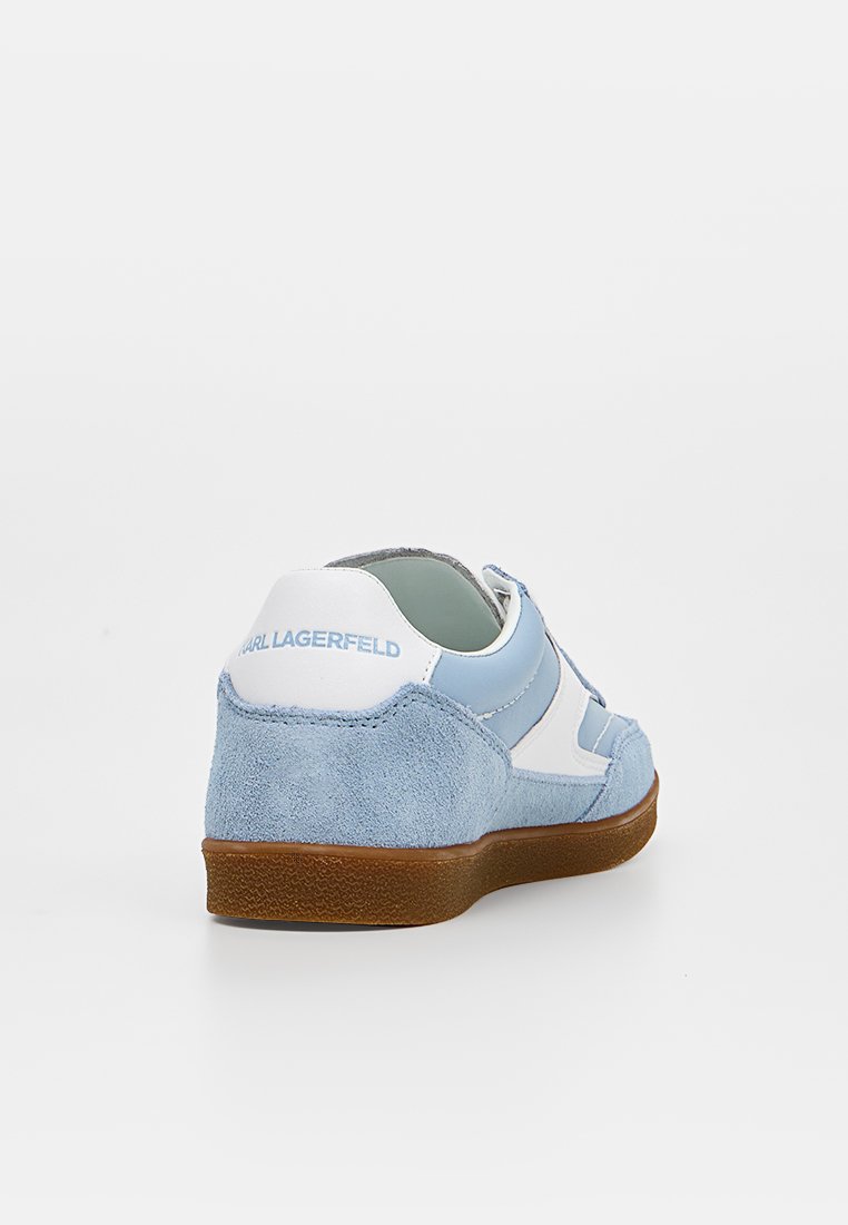 Zapatilla de ante azul claro y blanco con suela marrón, vista desde detrás a la derecha, con la marca "Karl Lagerfeld" en la lengüeta del talón.