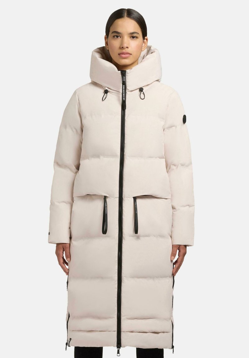 Light pink puffer coat featuring a high neck, zip front, and side zippers. It has large puffed sections and a hood for added warmth.