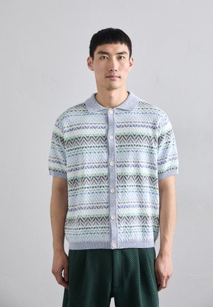 Short-sleeved knit cardigan in light blue with multicolored zigzag and stripe patterns. Features a button closure and a soft collar.