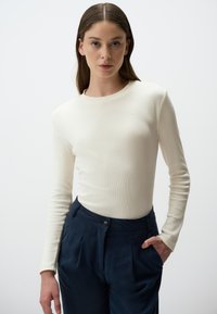 Maglietta a maniche lunghe in crema con costine abbinata a pantaloni navy a vita alta, caratterizzati da un dettaglio con bottone e tasche laterali. Design pulito e testo liscio.