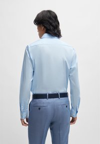 Camisa de manga longa azul clara com punhos abotoados, tecido suave. Combinada com calças texturizadas azul claras, com bolsos traseiros e um cinto escuro.