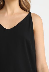 Top negro sin mangas con diseño de escote en v. Tela suave y ligera con un ajuste relajado. Presenta tirantes delgados en los hombros.