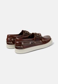 Braune Lederbootschuhe mit weißen Gummisohlen, kontrastierenden Nähten, Schnürdesign und Metallösen.