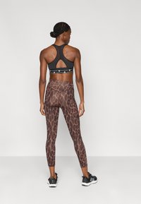 Μαύρο αθλητικό σουτιέν με σχέδιο racerback, συνδυασμένο με καφέ κολάν με λεοπάρ μοτίβο. Μαύρα αθλητικά παπούτσια ολοκληρώνουν την εμφάνιση.