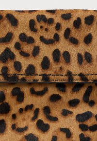 Detailný záber hnedo-čierneho leopardieho vzoru s viditeľným čiernym stehom pozdĺž švu zloženého povrchu.