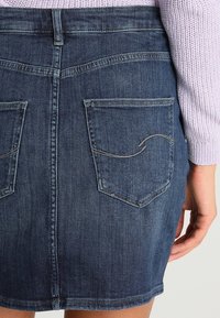 Spódnica dżinsowa w ciemnoniebieskim kolorze, z dwoma tylnymi kieszeniami o zaokrąglonych krawędziach i kontrastowym szwem. Długość do połowy uda, o dopasowanym kroju.