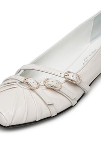 Scarpa piatta in pelle bianca con punta plissettata, tre fasce decorative con dettagli dorati e una fodera interna liscia.