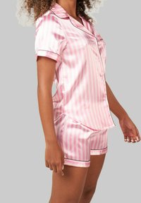 Ensemble de pyjama en satin rayé rose, composé de manches courtes et de shorts, rehaussé de garnitures noires le long des bords pour un détail supplémentaire.
