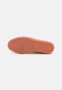 Zool van een sneaker in matte koraalrubber; heeft verhoogde cirkelvormige en patroontexturen voor tractie en grip. Gestempeld merlogo zichtbaar.