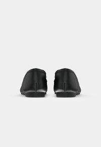 Black leather ballet flats with a smooth texture, rounded toe, low profile, and minimalistic design. Laces and stitching details visible.