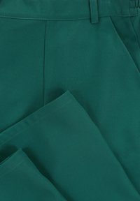 Donkergroene stoffen broek met een gladde textuur, gestructureerde taille en gedeeltelijk opgevouwen pijpen voor detail en ontwerphelderheid.