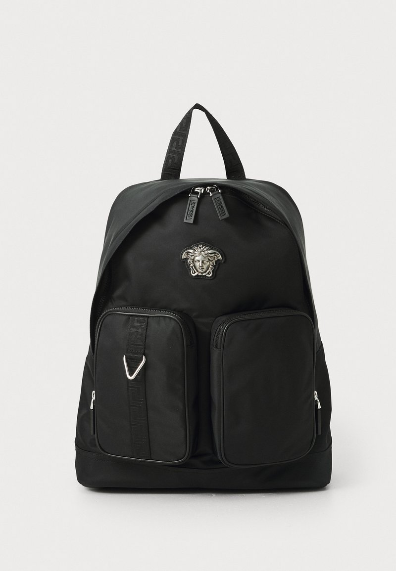 Mochila de nylon negra con un logo texturizado, dos bolsillos delanteros con cremallera y asas dobles en la parte superior. Presenta un diseño elegante y acentos de hardware en contraste.