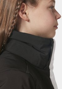 Černobílá zipová bunda s vysokým límcem a hladkým, matným povrchem. Boční profil ukazuje zapletené vlasy a detailní švy.