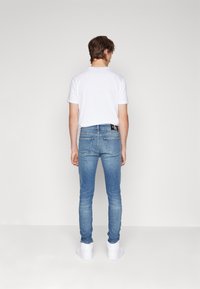 Smal blå jeans i denim med en lätt blekning. Har två bakfickor och en svart etikett med vitt logotyp vid midjan. Vit t-shirt och sneakers.