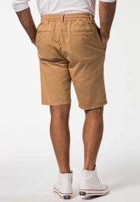 Brune shorts med elastisk talje, sidelommer og to baglommer. Bæret med hvide høj-top sneakers. Glat tekstur.