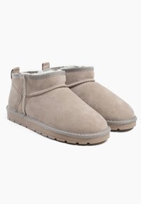 Las botas de tobillo de ante beige presentan un forro interior suave, una punta redondeada y un ribete gris. La suela tiene textura para ofrecer un mejor agarre.