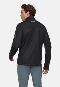 Schwarze Softshelljacke mit hohem Kragen, langen Ärmeln und Logo auf dem Rücken. Verfügt über Reißverschlusstaschen und eine taillierte Passform.