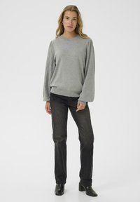 Un pull gris avec des manches ballon texturées et à motifs, associé à un jeans noir ajusté et des bottines à talons, sur fond clair.