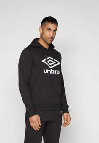 Čierna mikina s kapucňou vyrobená z bavlnenej zmesi, s veľkým bielym logom "Umbro" vpredu, klokaniu vreckom a rebrovanými manžetami.
