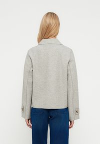 Giacca in misto lana grigia con colletto, forma leggermente corta e polsini con bottoni. Texture liscia, design minimalista e senza motivi visibili.