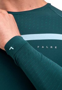 Ciemnoturkusowa, długorękawowa koszulka sportowa z teksturowanym rękawem, subtelnym kropkowanym wzorem i jasnoniebieskim poziomym paskiem. Widoczne logo marki "FALKE".