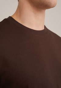 Camiseta de algodón marrón con mangas cortas y cuello redondo. Textura suave con un diseño ligero y ajustado, adecuado para el uso casual.