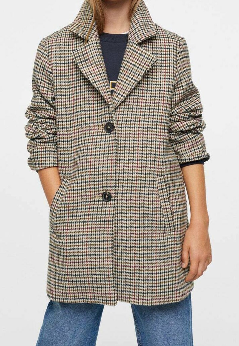 Ruudullinen takki, jossa on uurrettu kaulus, kolme nappia ja kaksi sivutaskua. Valmistettu tekstuurillisesta kankaasta, jossa on beigen, punaisen ja mustan sävyjä.