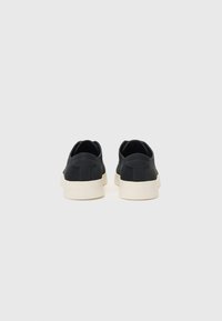 Zapatillas negras con parte superior de cuero liso, suelas de goma, una entresuela crema en contraste y un detalle de costura mínimo. Diseño trasero sencillo.