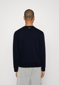 Sudadera azul marino de manga larga, cuello redondo, puños acanalados y un pequeño logo verde en la parte posterior. Material cómodo de mezcla de algodón.