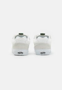 Baskets blanches en cuir et daim avec une semelle plate, des accents verts, et la marque "VANS" sur le talon et la languette. Panneau arrière texturé.