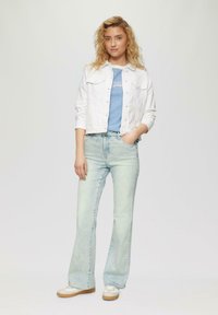 Witte denim jacket over een blauw gestreept shirt, gecombineerd met lichtblauwe flared jeans en crèmekleurige sneakers. Kenmerken zijn onder andere knoopsluitingen en zakken.