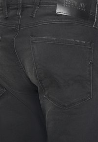 Jeans de denim negro con un diseño elegante, desvanecimiento sutil y costuras en tono. Incluyen un bolsillo trasero con un patrón distintivo en forma de zig zag.