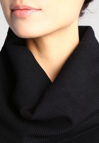 Col roulé en tissu côtelé noir, gros plan montrant la texture douce et le drapé. Design minimaliste sans embellissements. Peau lisse en arrière-plan.