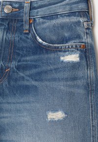 Džíny kraťasy ve světlé modré barvě s odřenými detaily, s roztrhanými okraji a oranžovým prošíváním poblíž kapes a pasu.