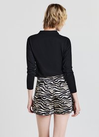 Top a maniche lunghe nero abbinato a pantaloni corti a vita alta con stampa zebra in nero e beige, che mostrano una texture liscia e una vestibilità sartoriale.