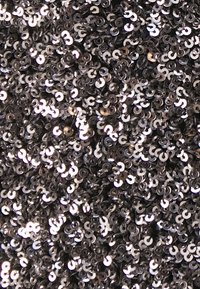Paillettes noires et argentées à surface brillante, présentant une forme circulaire et des reflets complexes, densément disposées dans un agencement texturé.