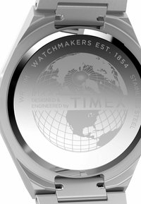Fond en acier inoxydable avec un design de globe. Texte gravé comprenant "Horlogers Établi en 1854" et "Conçu et Ingénierie par Timex."