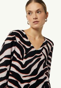 V-Ausschnitt-Oberteil aus Stoff mit einem schwarz-weißen Zebra-Print und orangefarbenen Akzenten; mit langen Ärmeln und entspannter Passform.