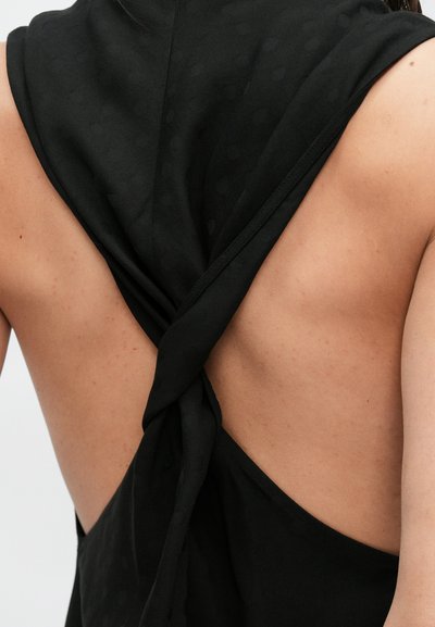 Černý tílko bez rukávů s propleteným zadním designem, hladkým materiálem a otevřenými zády. Na látce je viditelný jemný vzor drobných teček.