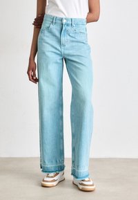 Lyseblå denim vide bukser med høj talje, frynsede kanter og to frontlommer. Sammen med hvide sneakers med brune accenter.