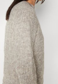 Beżowy sweter dziany z teksturowanym wzorem, szerokimi rękawami i okrągłym dekoltem. Miękki materiał o przytulnym wyglądzie.