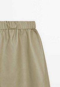 Jupe beige en similicuir avec taille élastiquée froncée, texture lisse, sans motifs ni décorations visibles.