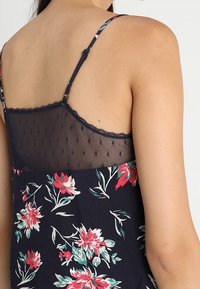 Top senza maniche con motivo floreale in blu navy, caratterizzato da un pannello in rete trasparente sul retro con texture a pois e spalline regolabili.