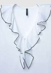 Blusa bianca con scollatura a V profonda e colletto arricciato rifinito con un bordo nero, realizzata in tessuto liscio. Dettaglio centrale con bottoni visibili.