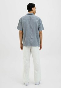Cămașă cu mânecă scurtă, gri deschis, texturată, cu guler, asortată cu pantaloni albi cu croi larg și adidași albi, văzută din spate.