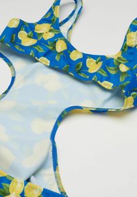 Blauer Badeanzug mit Zitronenmotiv, gefranstem Ausschnitt und überkreuzten Trägern. Glatte Textur mit kontrastierenden gelben und grünen Akzenten.