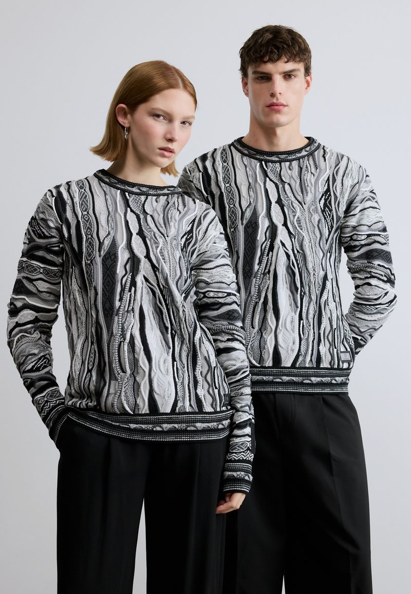 Pulls tricotés à motifs en noir et blanc avec manches longues, présentant des designs texturés et des finitions noires contrastantes, assortis à des pantalons décontractés.