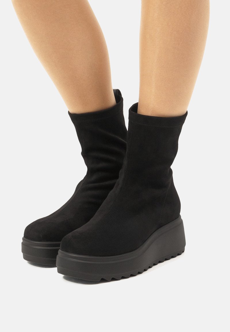Botas de tobillo de ante negro con una textura suave, forma cónica y una suela de plataforma gruesa y contrastante que presenta un patrón en zigzag.