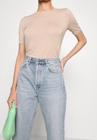 Camiseta de punto beige con mangas cortas, combinada con unos jeans de tiro alto en azul claro, complementada con un bolso de mano verde.