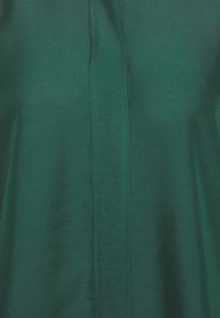 Gros plan d’un tissu vert avec une couture verticale centrale et des détails de surpiqûres subtils sur un matériau lisse.